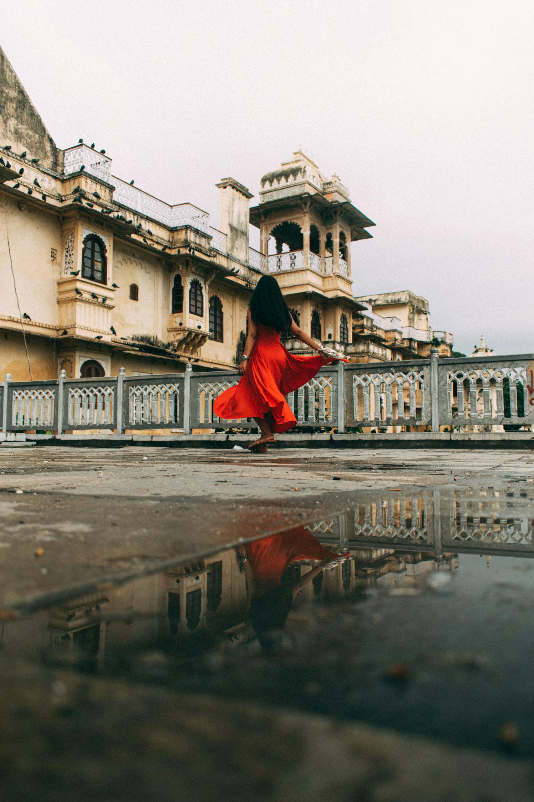 A woman in a red dress walks through the palatial architecture of Udaipur, India.