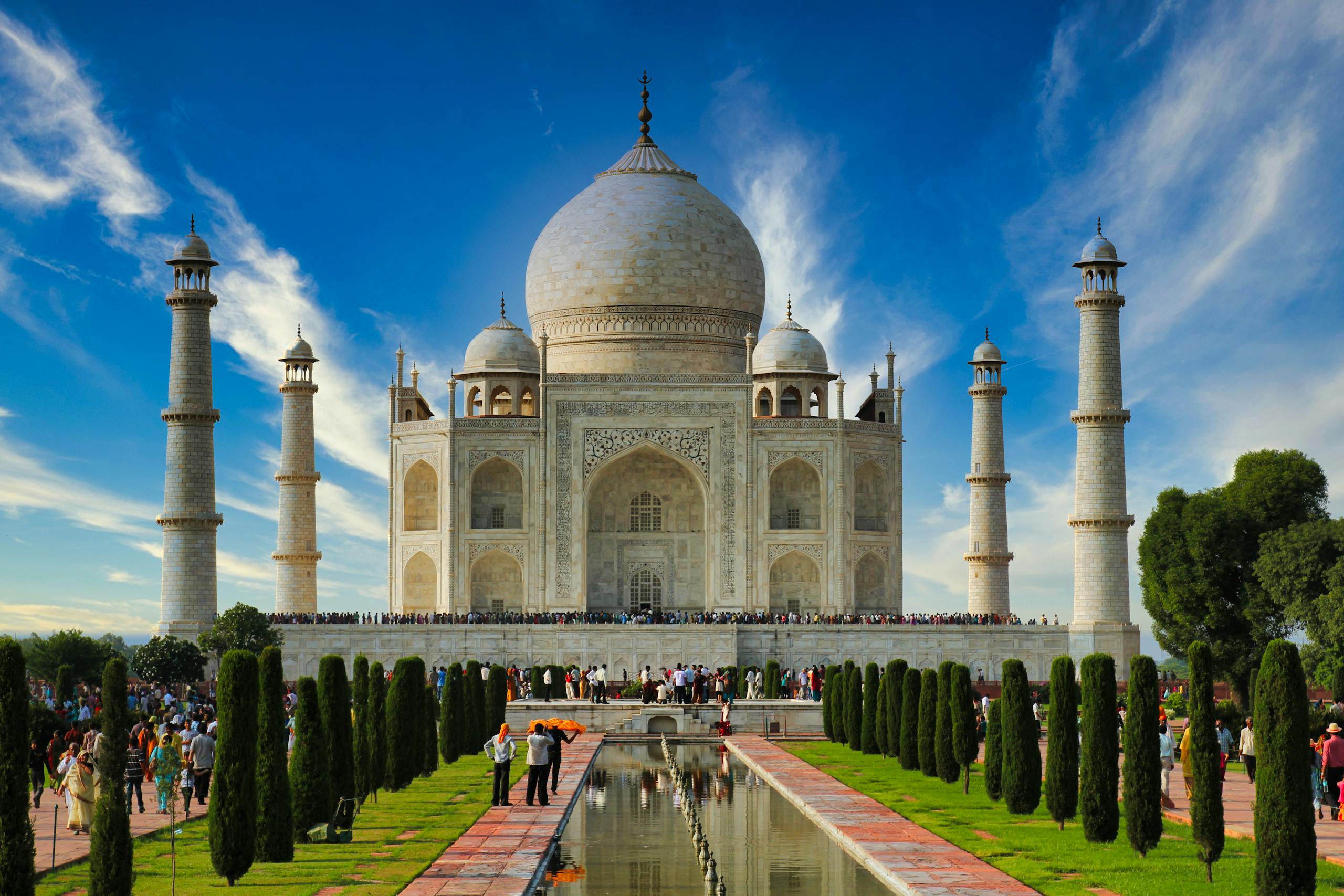 Stunning frontal view of the Taj Mahal under a clear blue sky with tourists exploring the iconic landmark.
